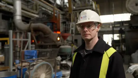 BBC News / Kevin Church Image of scientist Dr.  Cyrille Dunant standing in front of the arc furnace at the Materials Processing Laboratory in Middlesborough.  The oven is glowing red hot.